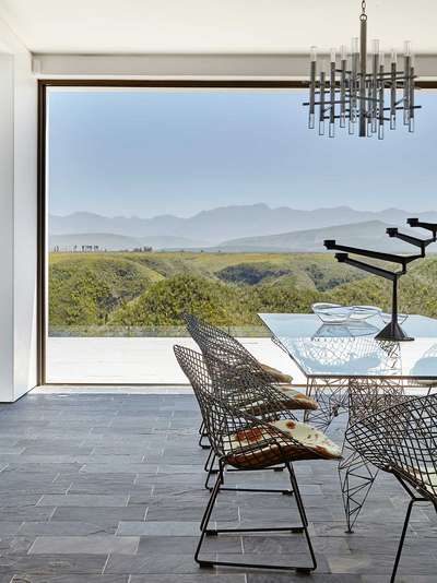 Neben dem Panoramafenster offenbart auch Tisch »Pylon« von Stardesigner Tom Dixon beeindruckende Aussichten auf dem metallischen Gestell. Abgerundet wird das Gesamtbild durch die Stühle von Harry Bertoia.